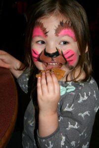 A cute little girl with an adorable face painting eating a cookie