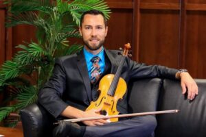 A violinist sitting on a chair while holding a violin