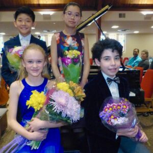 Four young orchestra members holding bouquets of flowers